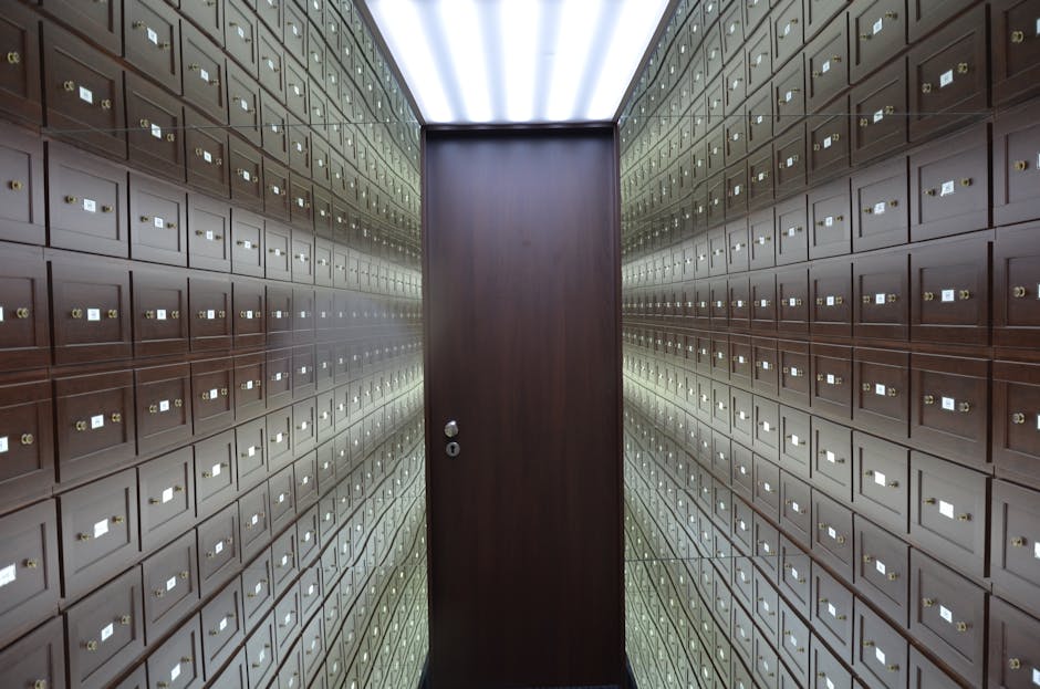 Inside a facility with walls covered in numerous small, uniformly arranged brown metal postboxes, each secured with a small lock, leading to a dark wooden door at the end of the corridor. The lighting is artificial, casting a neutral illumination over the postboxes, which are organized in neat rows across both walls. The scene appears to be a secure postal or storage area, possibly part of a home relocation or moving process, with no visible furniture or packaging materials. The environment suggests a controlled space for storing or retrieving household items, fitting within the context of professional removals and moving services offered by Man and Van Pimlico.